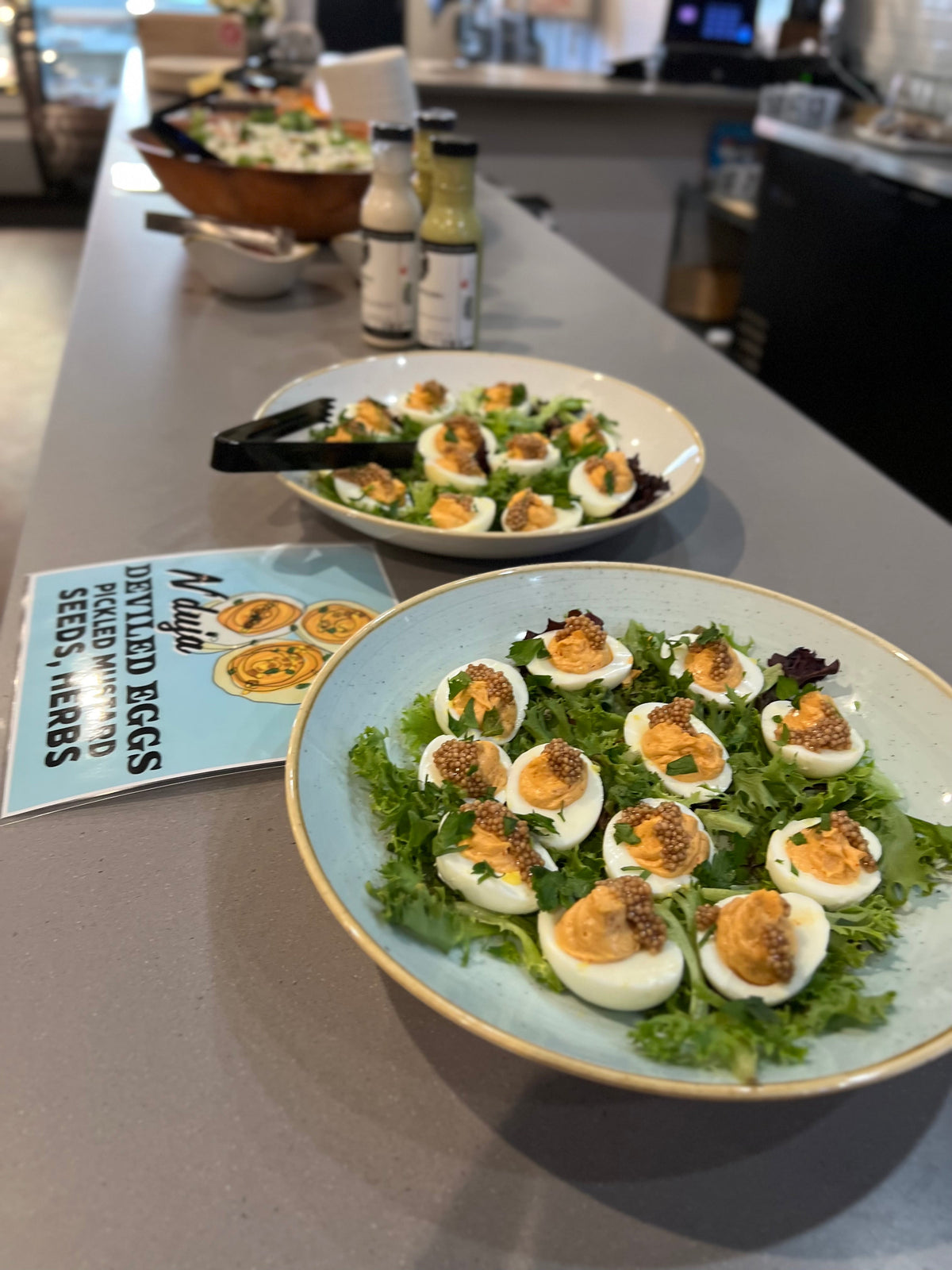 Platters of N'duja deviled eggs on greens, topped with pickled mustard seeds and herbs