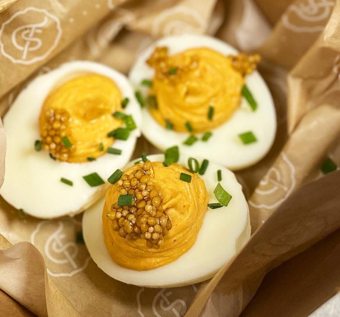 Three N'duja deviled eggs topped with pickled mustard seeds and chives